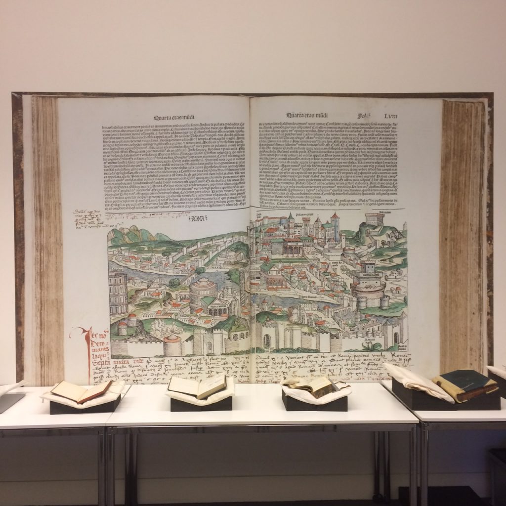 Four archival books on a table set to a backdrop of a giant book.