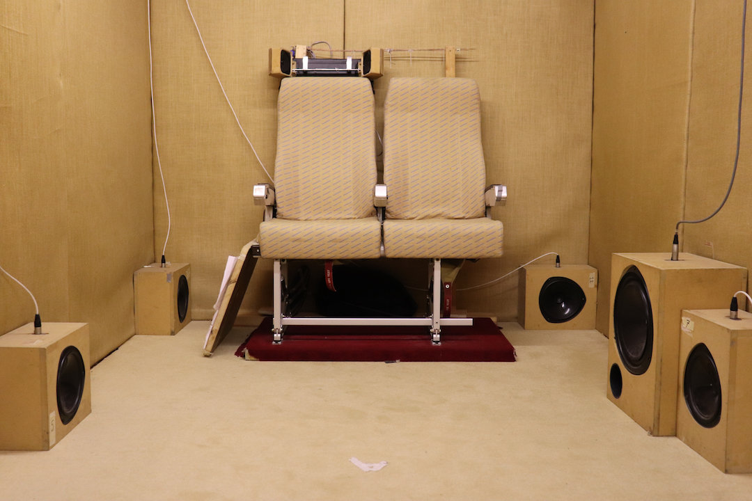 A small room with two airline chairs and multiple speakers which is used to test airport noise pollution.